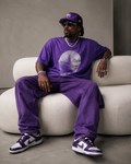 Model wearing a purple GlitchMan graphic T-shirt in a modern interior